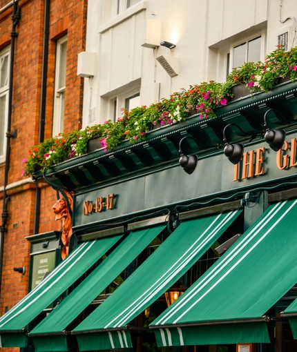 A close up view of the exterior facade and signage of The Globe in Marylebone; with large green awnings, and flower boxes at the upper floor.