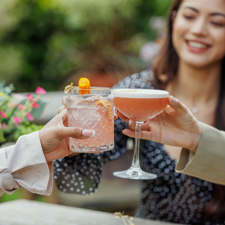An exterior image of a group of people celebrating with a cheers with various cocktail style drinks available at Crafted venues.