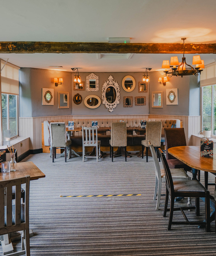The interior restaurant seating area of The Green Man, with an upholstered booth seat, framed artwork and mirrors on the wall, and wooden beams.