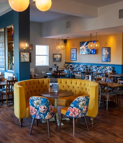 The interior restaurant seating area of The Kittoch in East Kilbride, with upholstered booth seats, and framed artwork and a TV on the wall.