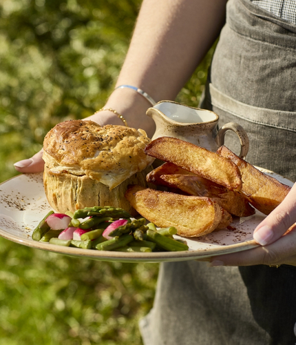 Hands holding a plate of pie, potato wedges and vegetables.