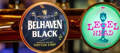 A close up view of beer taps for Belhaven Black, Level Head, and Hazy Day, on the bar inside The Merlin.