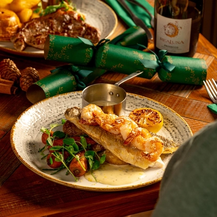A wooden table, decorated with festive decoration is  holding a plated seabass dish.