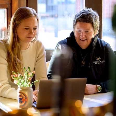 Two Women sat at a table looking at a laptop