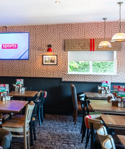 The interior restaurant seating area at The Bramford Arms in Woodsetton; with a long, upholstered booth seat along one side of the room, and a TV on the wall.