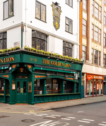 The exterior facade and signage of The Golden Lion in Soho, with a large clock on the wall and flower boxes at the upper windows.