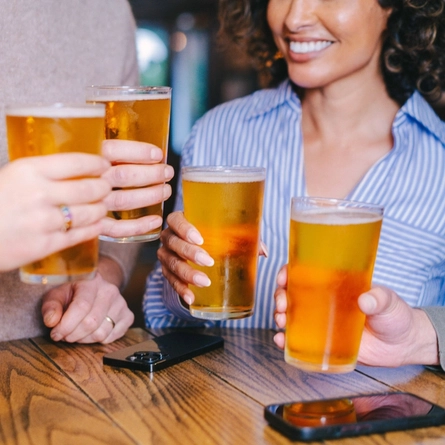 A close up view of four hands raising glasses of cider at a table in a pub.