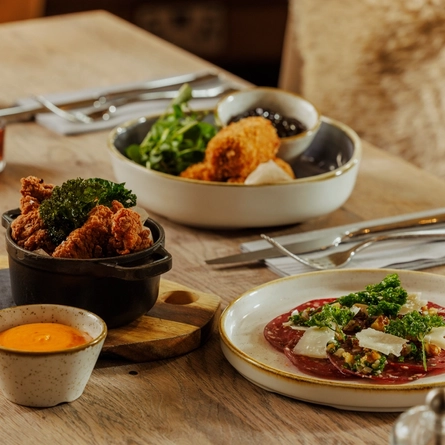 An advertising image of 3 Game Night Starter dishes and a glass of red wine within the interior restaurant and seating area at The Foundry Bell.