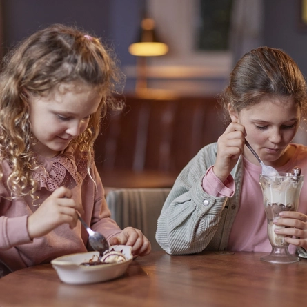 Two girls sitting at a table together and eating ice cream.