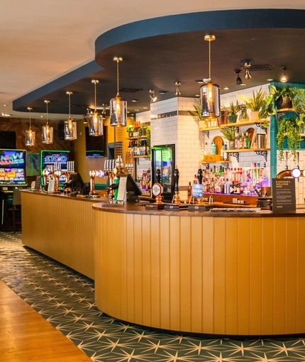 The bar area inside The Merlin in Edinburgh, with wooden tables and chairs, and pub game machines.