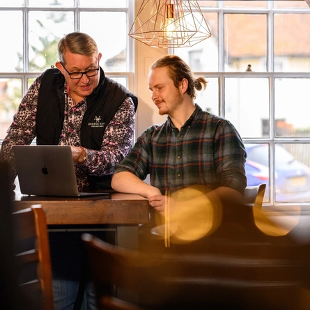 two men sat at a table looking at a laptop