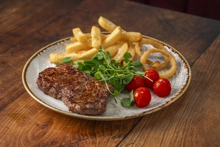A plate of steak, chips, onion rings and salad, sitting on a wooden table.