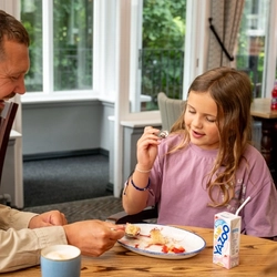 An image of a young girl enjoying a dessert and drink with her father,  within the interior restaurant and seating area at a Hungry Horse venue.