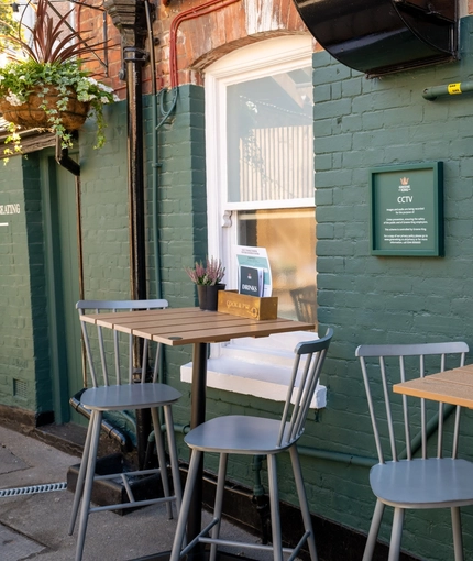 The exterior seating area of the Cock & Pye, with menus and flowers on each table and flower baskets hanging on the wall.
