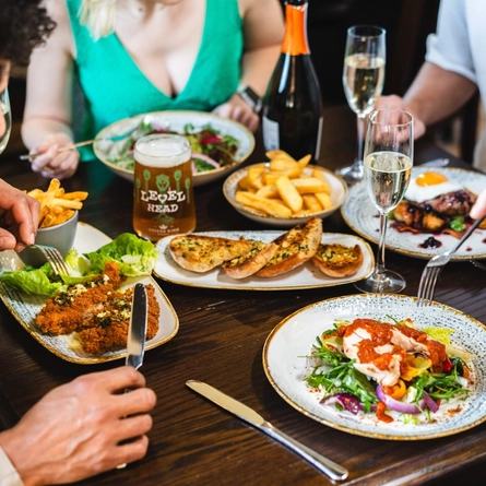 Lots of food on a table with drinks and people sat around