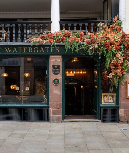 The exterior facade of the venue with historical information signage and Autumnal hanging floral decor at The Watergates Bar.