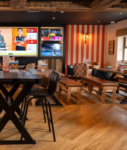 The interior restaurant seating area at the Arch & Anchor, with wooden tables, upholstered seats, and TVs on the wall.