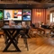 The interior restaurant seating area at the Arch & Anchor, with wooden tables, upholstered seats, and TVs on the wall.