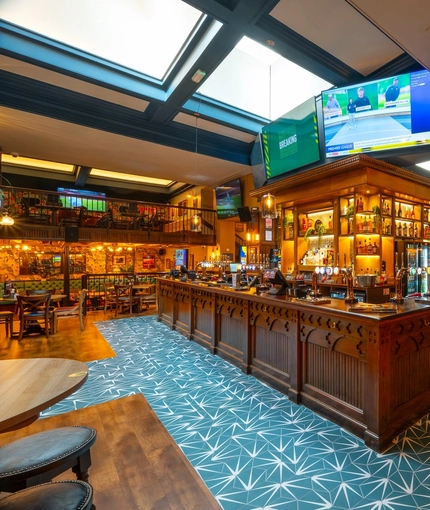 The bar area inside the Old School House, with TVs on the wall above the bar, large sky lights in the ceiling, and views of the restaurant seating areas on the upper and lower floors.