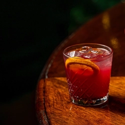 Two cocktail type drinks on a bar.  One in a low ball tumbler and the other is in a stemmed glass.