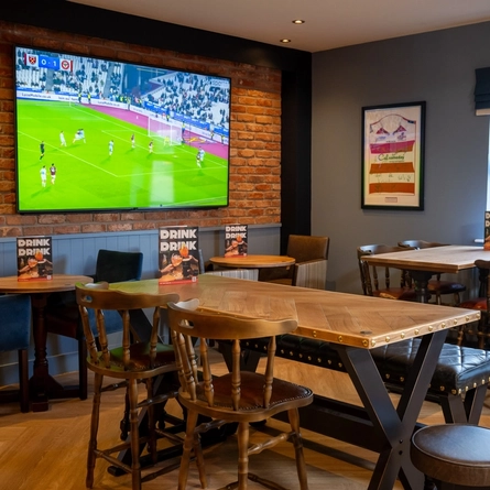 The interior restaurant seating area of The Parsonage in Leigh, with wooden tables and a TV on the wall.