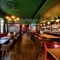 The bar and interior restaurant seating area at the King's Head, with dark wood floors; green, textured wallpaper on the ceiling; and a long, red, upholstered booth seat along one wall by the window.