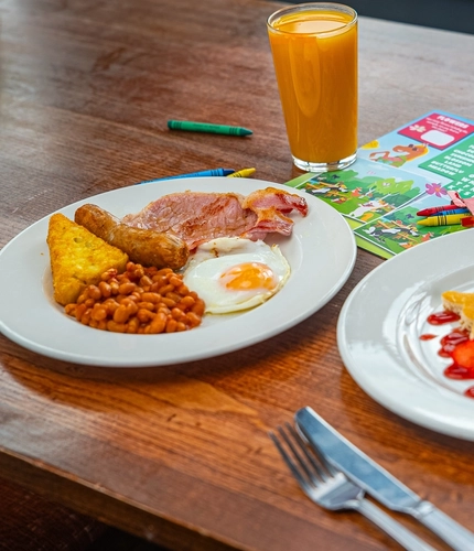 A plate with a pancake in the shape of a bunny rabbit with strawberries and a plate with a full English breakfast.