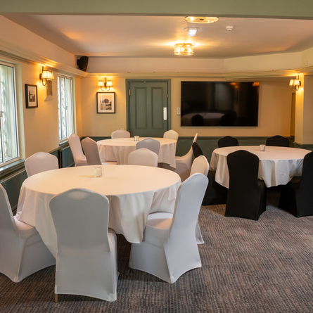 The function room at The Blue Cap, with three large, circular tables covered in white table cloths, and a TV on the wall.