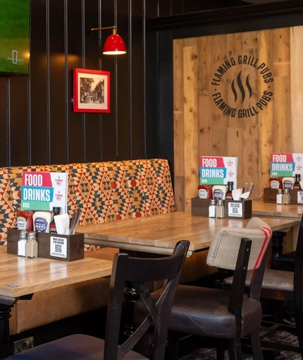 An interior restaurant seating area at The Amington in Tamworth; with a long, upholstered booth seat along one side of the room, and a TV on the wall above it.