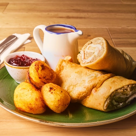 A turkey, stuffing and cranberry wrap served with roast potatoes on a plate with a jug of gravy.