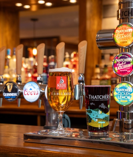 A close up view of the beer taps on the bar inside The Parsonage in Leigh, with a glass of beer and a glass of cider sitting on the counter.