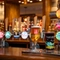 A close up view of the beer taps on the bar inside The Parsonage in Leigh, with a glass of beer and a glass of cider sitting on the counter.