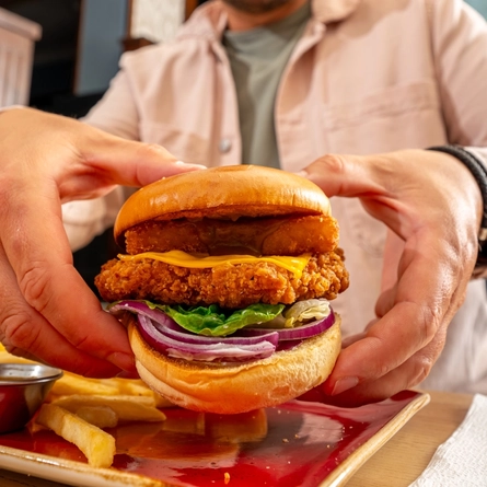 A close up image of a burger with a person in the background within the interior restaurant and seating area at a Hungry Horse venue.