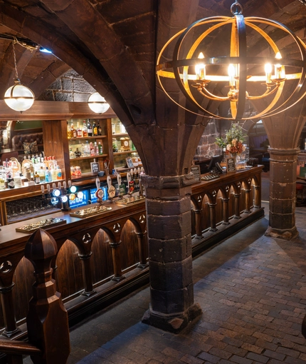 An elevated image showing the interior bar and restaurant seating area with wooden gothic arched carvings, tiled flooring and stone vaulted ceiling at The Watergates Bar.