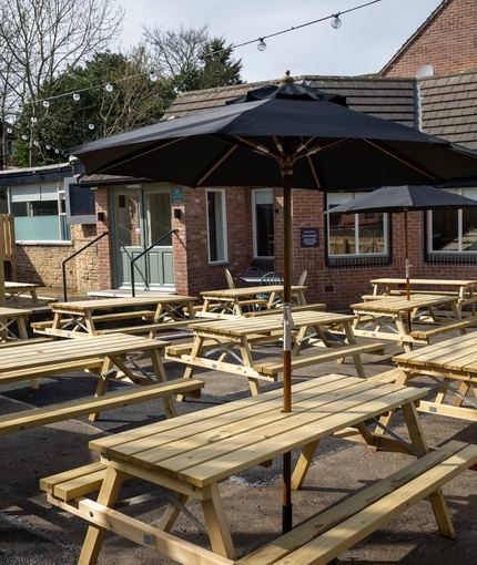 The exterior beer garden seating area at the Devonshire Arms in Sheffield, with wooden picnic tables, shade umbrellas, and string lights.