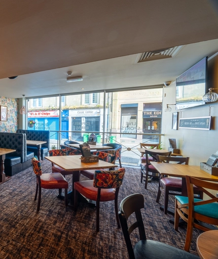 An interior restaurant seating area at the Counting House, with upholstered chairs and booth seats, and a TV on the wall.