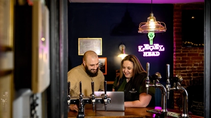 A Man and Woman leaning on the bar looking at a laptop and smiling.
