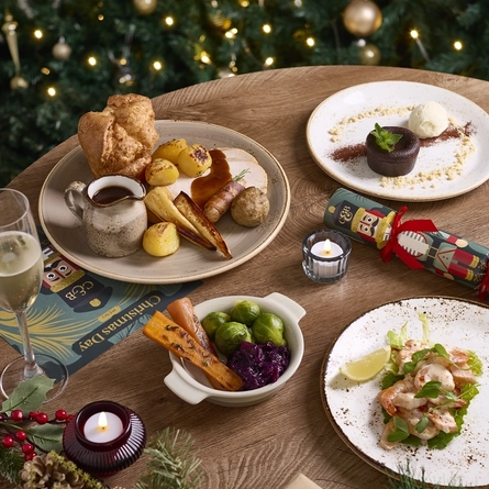 An advertising image showing Christmas Day dishes and a glass of sparkling white wine sat on a table within the interior restaurant seating area at a Chef & Brewer venue.