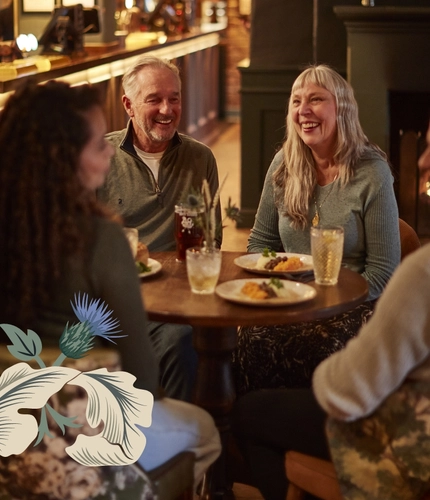 4 people sat around a table with drinks. In front of the fire and the bar.