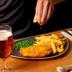 A hand squeezing a lemon wedge over a plated fish and chip meal.