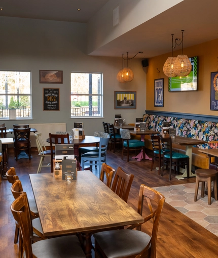 The interior restaurant seating area of The Kittoch, with a long, upholstered booth seat, a TV on the wall, and potted plants hanging from the ceiling.