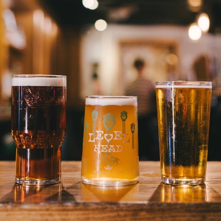 Three pint glasses containing ale and cider are lined up on a bar.
