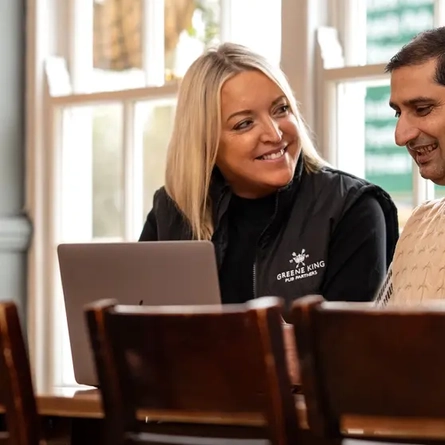 A Woman and a Man sat at a table looking at the laptop in front of them
