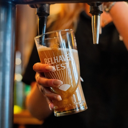 A close up view of beer taps on a bar and a bartender holding a glass and filling it with Belhaven Best ale.
