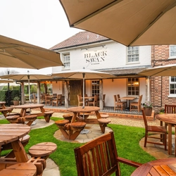 An image showing the exterior beer garden seating area with wooden tables complete with umbrella shades and chairs at The Black Swan.
