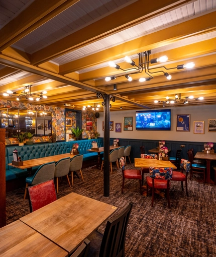 An interior restaurant seating area at the Old School House, with upholstered chairs and booth seating, and a TV and framed artwork on the wall.