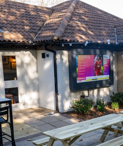 The exterior beer garden seating area at the Clocktower in Milton Keynes, with wooden picnic tables and string lights.