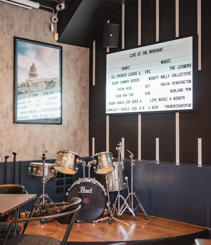 A small raised platform area with a drum kit on it. A board on the wall with information on it about up coming live events.
