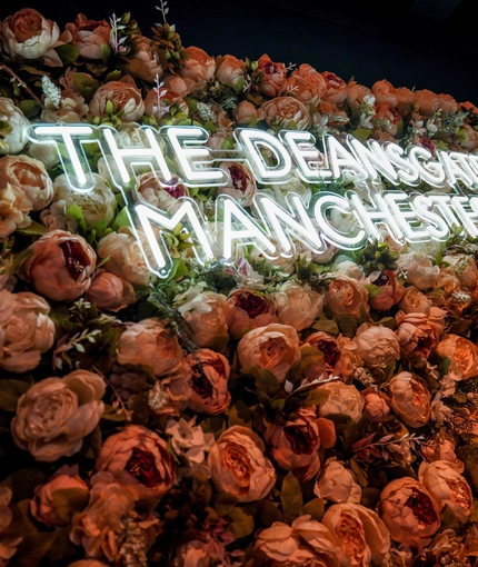 Neon sign saying Deansgate Manchester on a background of faux roses