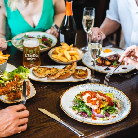 Lots of food on a table with drinks and people sat around